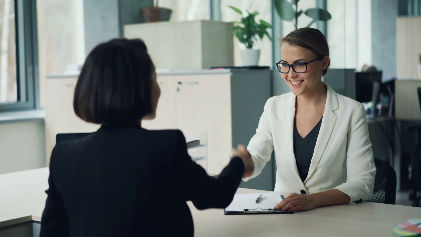 Two professionals shaking hands across a desk in a modern office