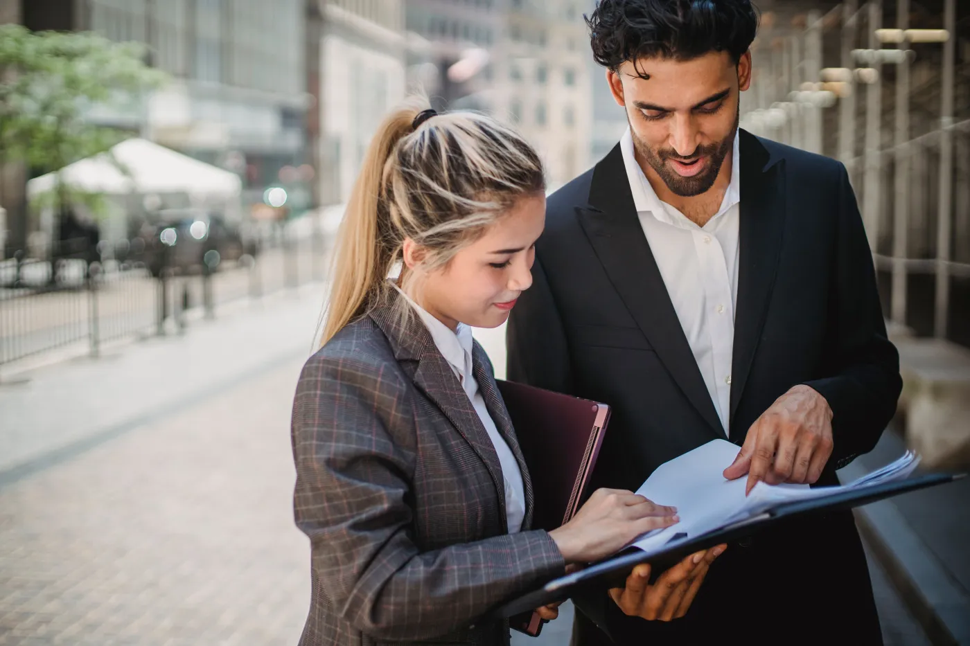 Two professionals reviewing documents in a folder outside a civic building