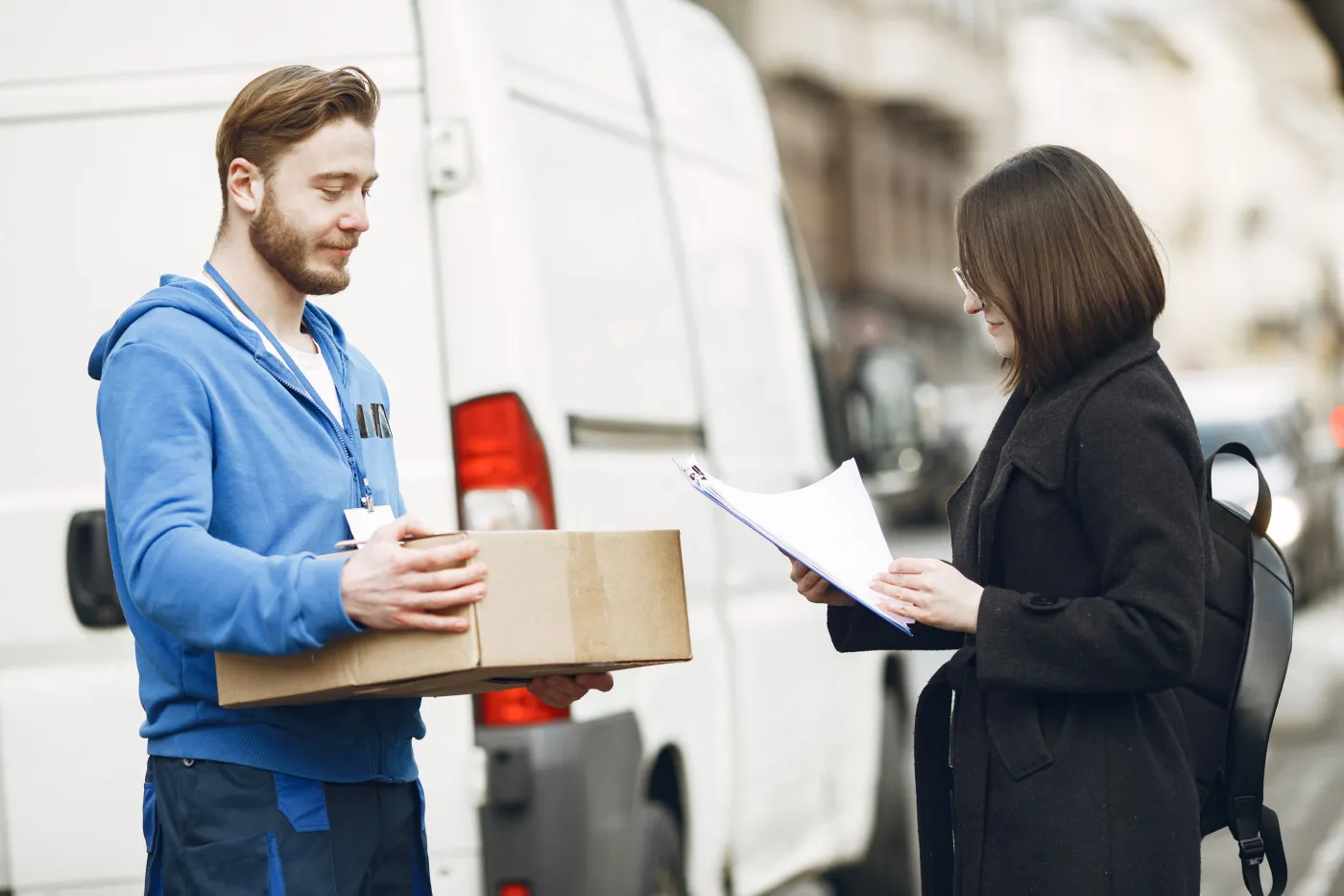 Courier handing off a package beside a delivery van while a customer reviews delivery paperwork