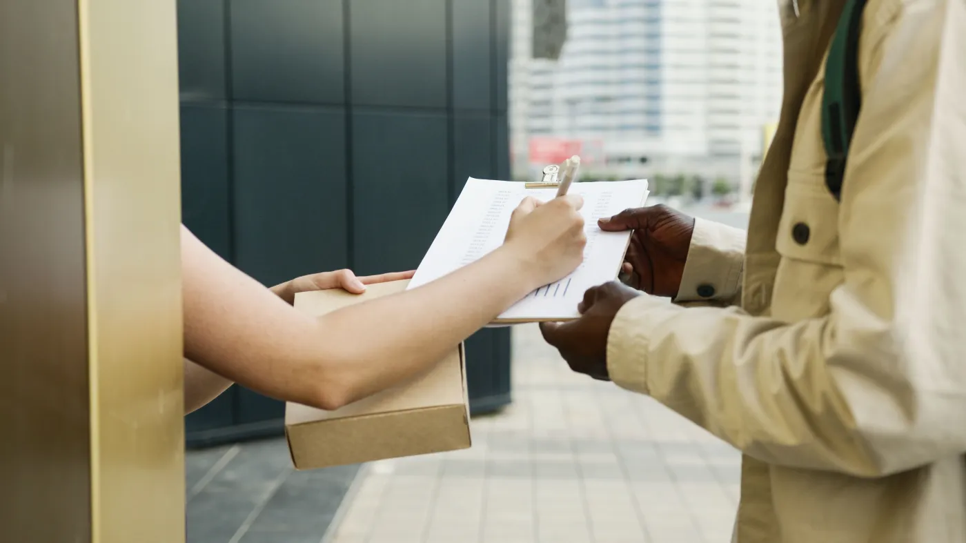 Customer signing a delivery form while receiving a package from a courier